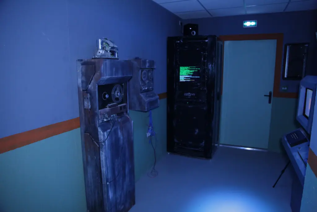 Salle informatique avec anciens ordinateurs et panneaux lumineux.