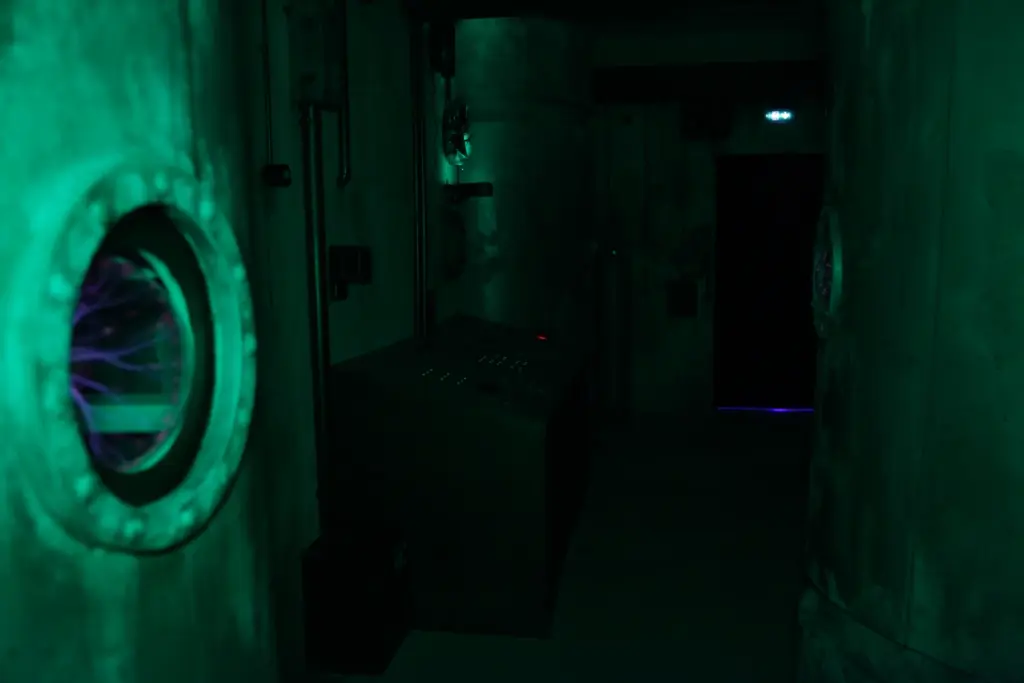 Salle industrielle sombre avec lueurs vertes, machines visibles.