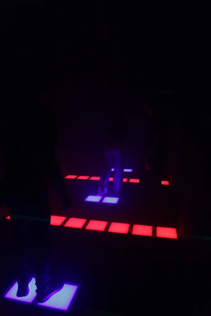 Personnes sur sol lumineux rouge et bleu, obscurité.