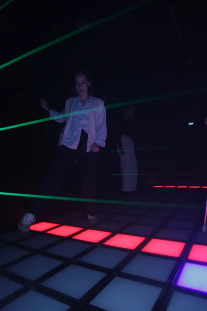 Danseuse sur piste lumineuse avec rayons laser verts.